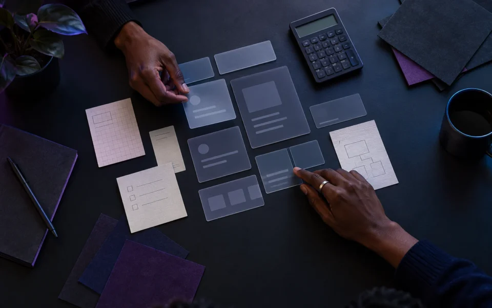 Two professionals arranging translucent interface cards and planning notes on a dark desk